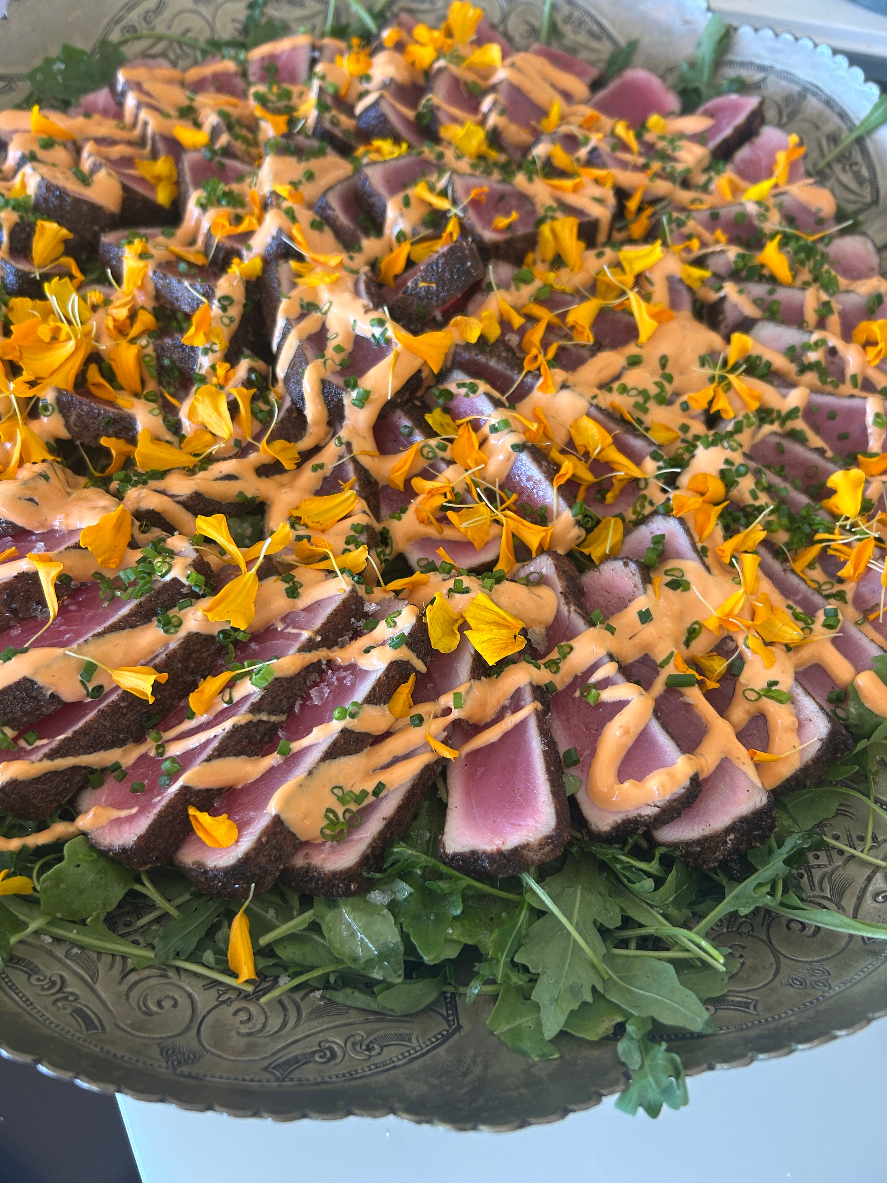 Plated dish with sliced purple fish, yellow flowers, and green leaves on a decorative plate.