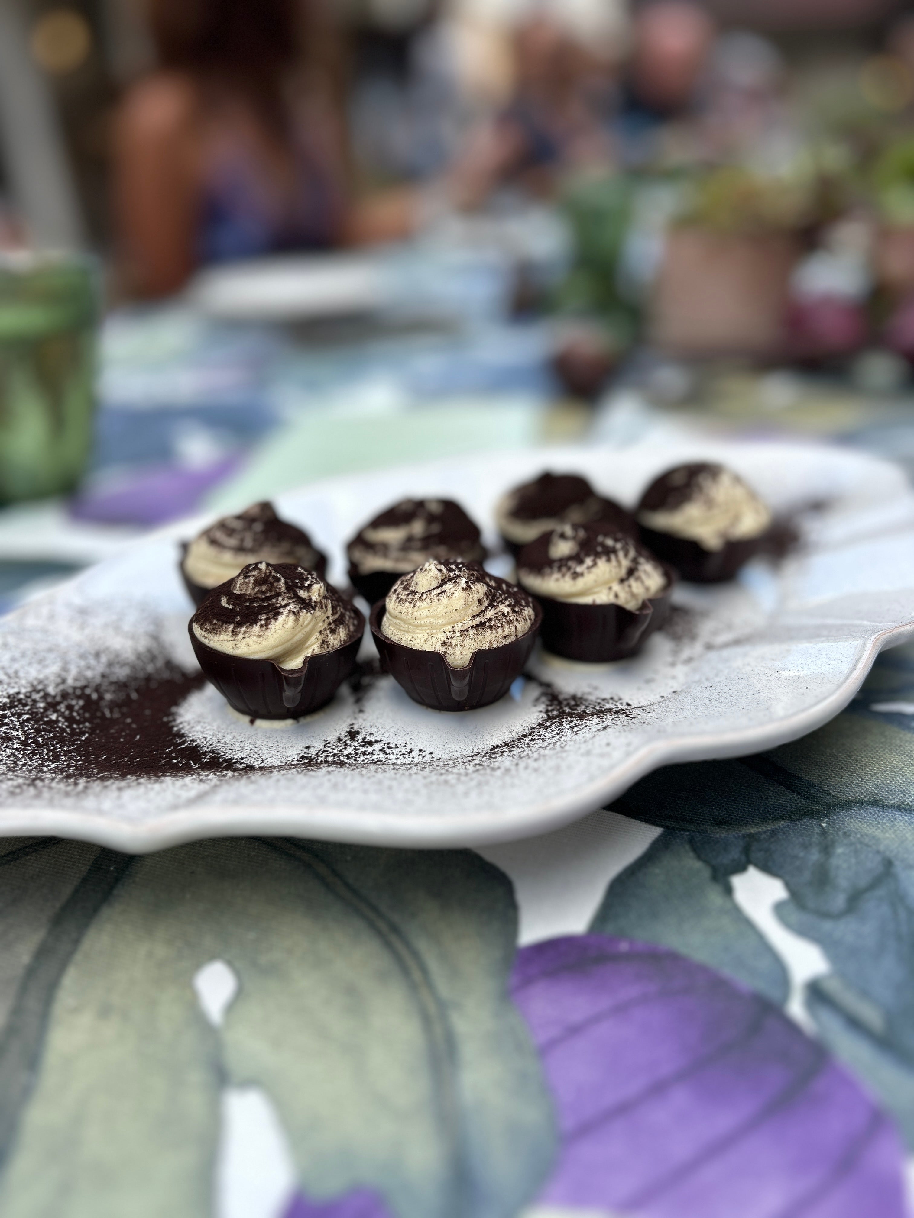 Small chocolate desserts with cream on a decorative plate outdoors.