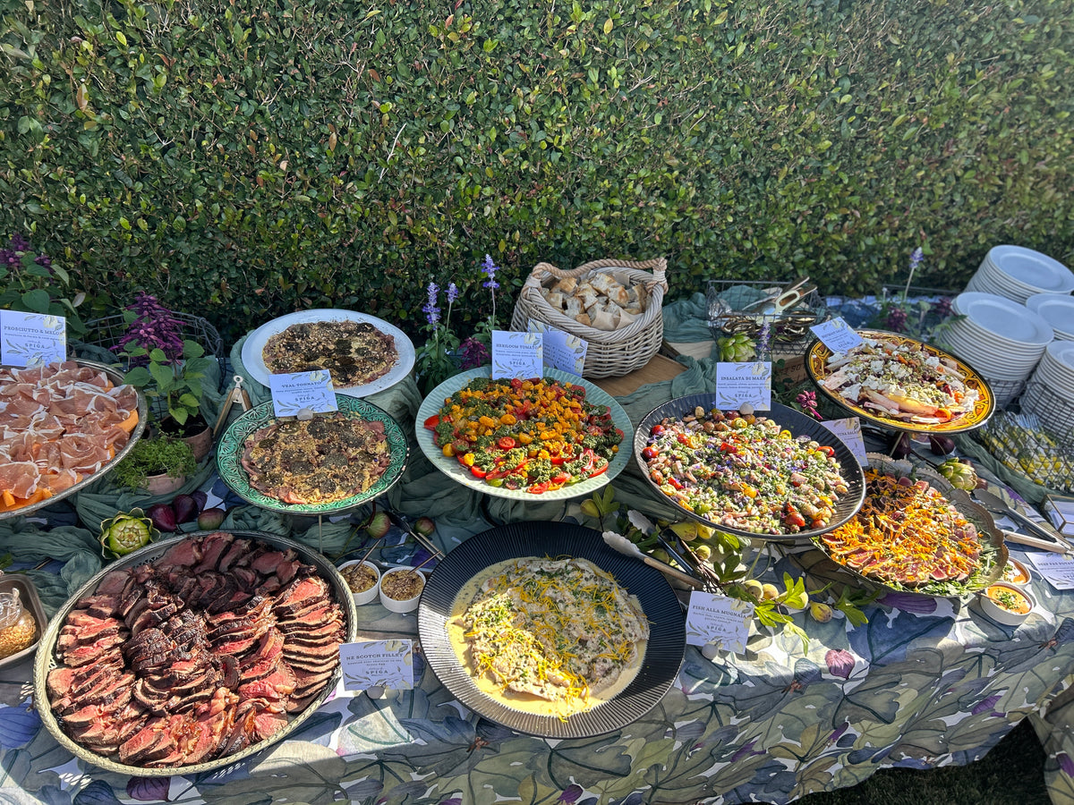 Outdoor buffet table with various dishes against a green hedge background