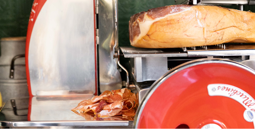 Sliced ham on a meat slicer with a visible brand logo.