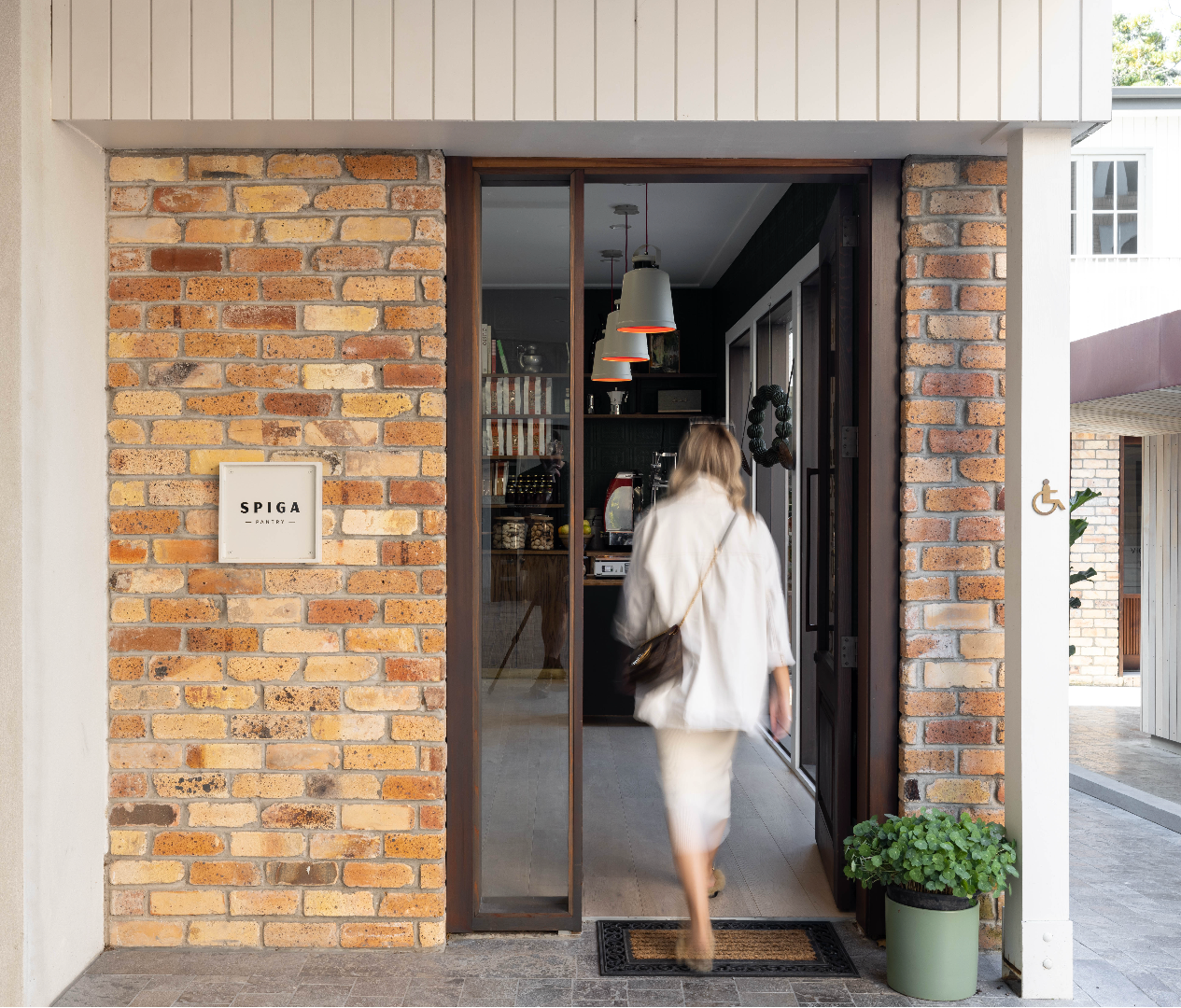 Woman entering a modern building with a brick facade and 'Spiga' sign.