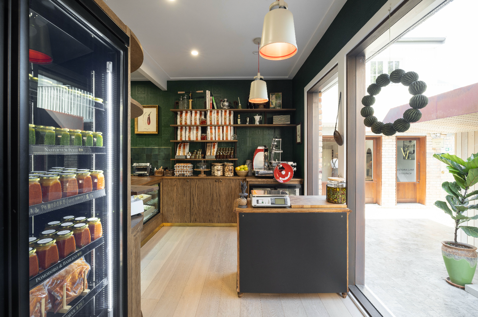 Interior of a modern cafe with a refrigerator displaying jars and a counter area.